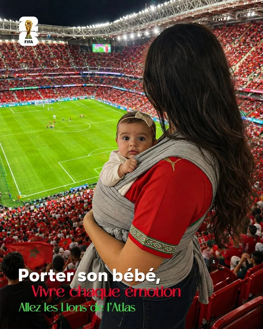 A baby-carrier campaign creative: a woman photographed from behind in a packed football stadium, carrying a baby in a grey woven wrap, under a French headline about carrying your baby and living every emotion.